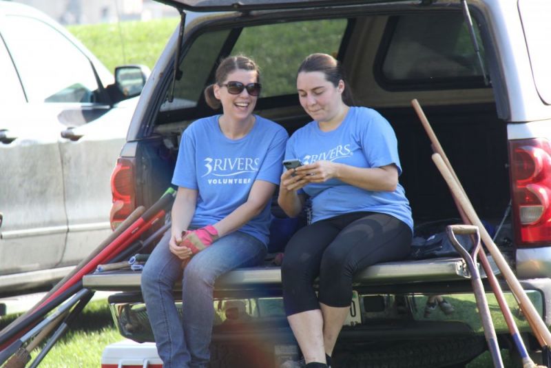 Two female volunteers sit in back of pick-up truck surrounded by yard tools.