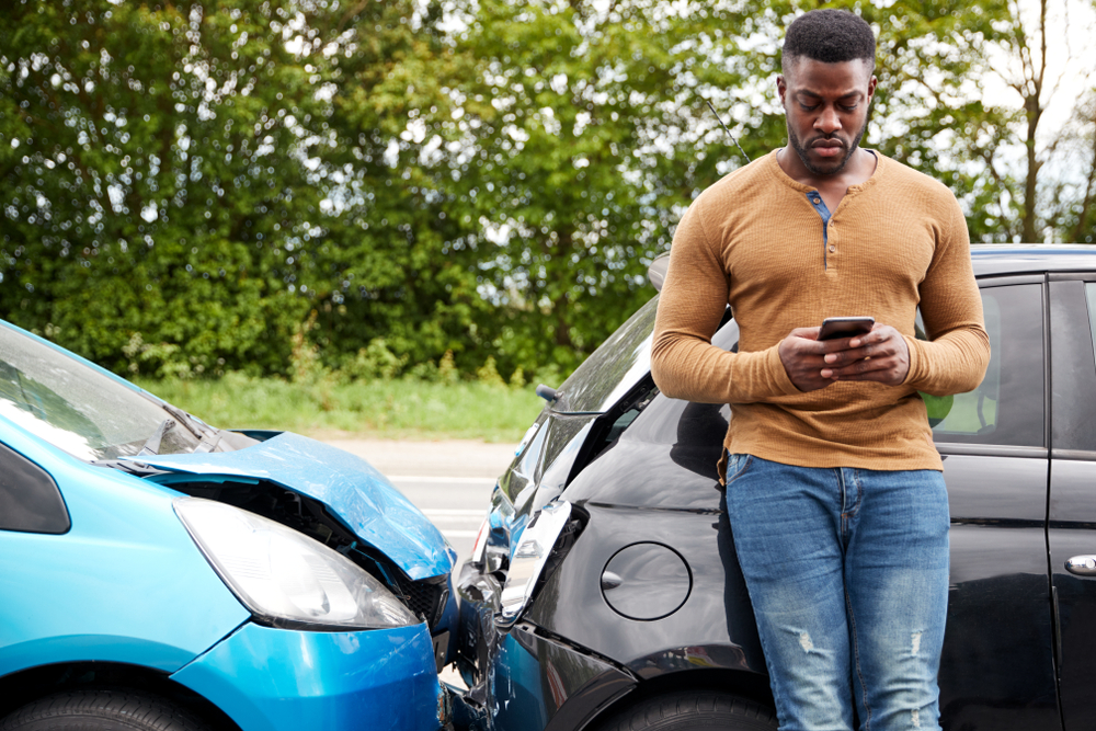 Man standing in front of car accident on phone.