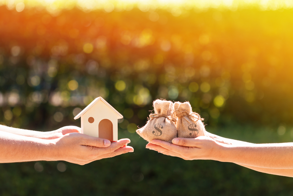 Hands holding a small house and money bags.