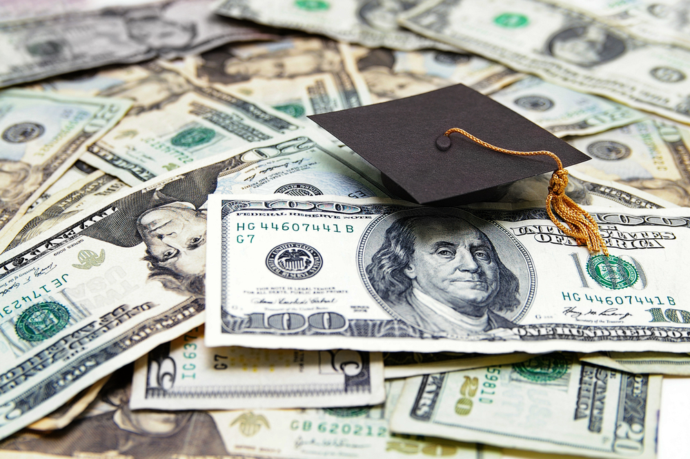 Pile of US paper currency with a graduation cap on top.