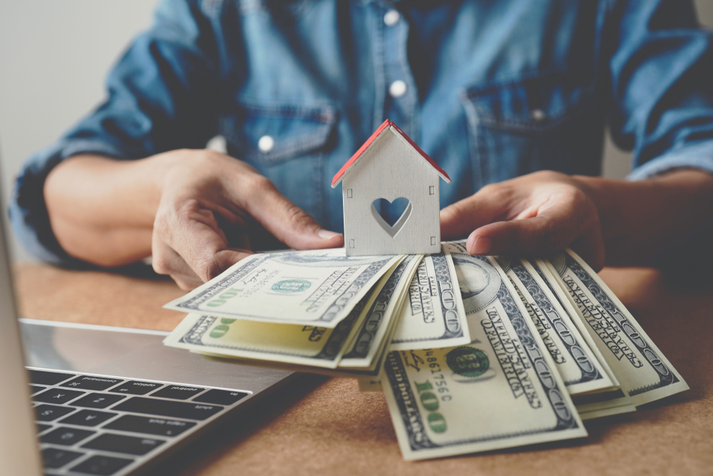 Hands holding cash and a wooden house.