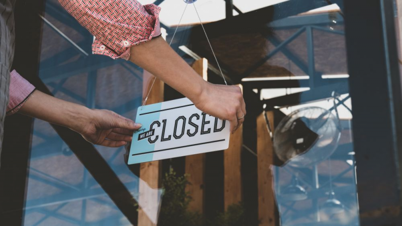 Close up of hands putting a closed sign on a business door.