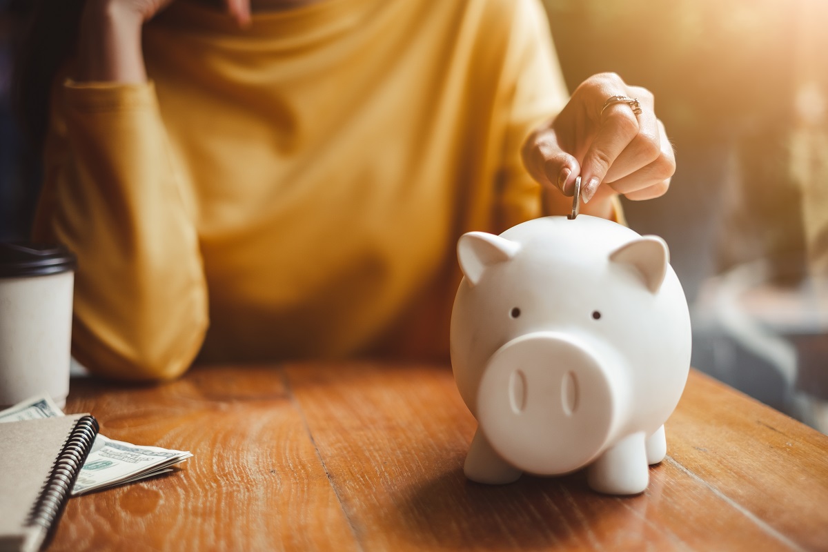 Close up of hand putting coin into piggy bank.