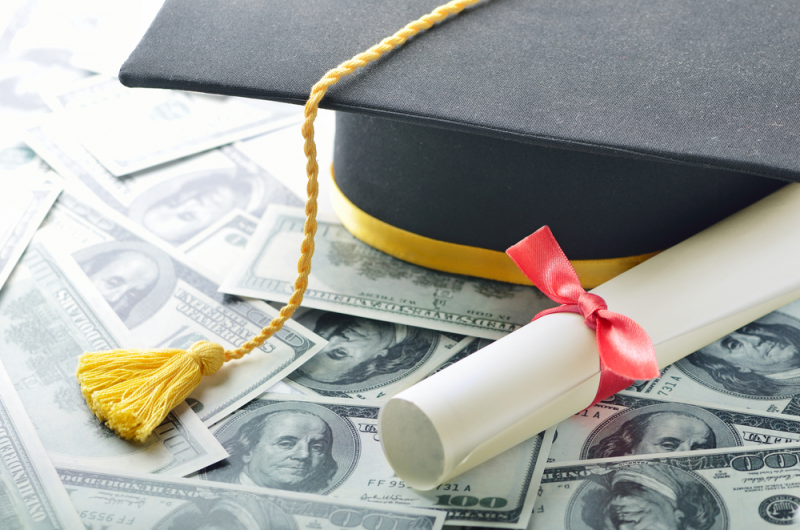 Graduation cap and diploma on top of one hundred dollar bills.