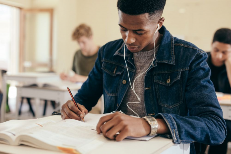 Student writing at desk while wearing headphones.