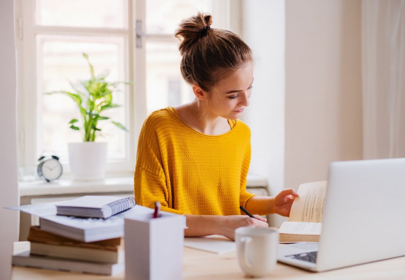 Young female working at desk, reading book.