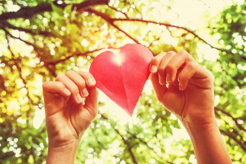 Hands holding a red paper heart in the air.