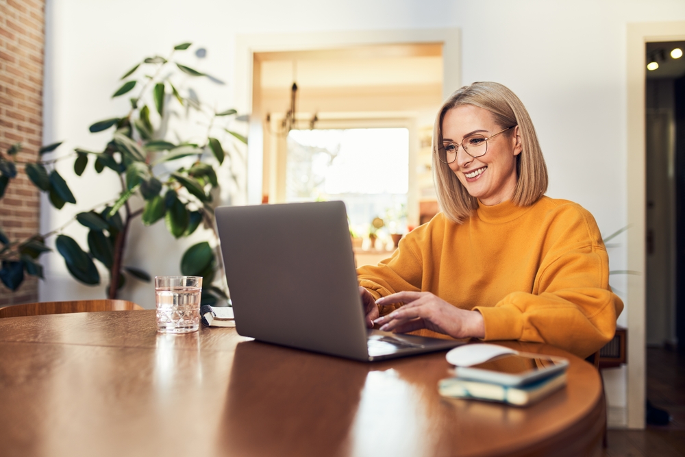 Woman at dining table, looking at laptop.