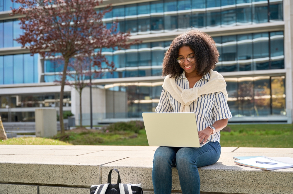 A college student sitting outside looking at a laptop.