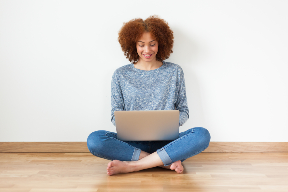 Young woman sitting on floor against wall using a laptop.
