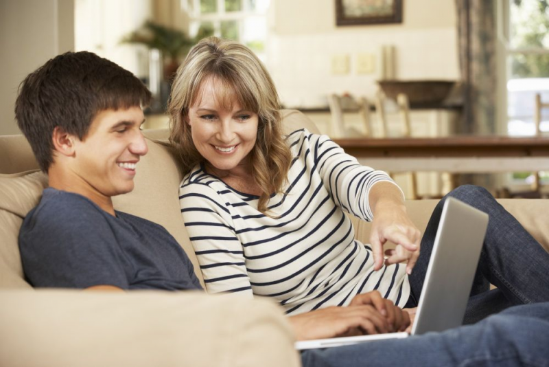 Mother and son sitting on couch, looking at a laptop screen.
