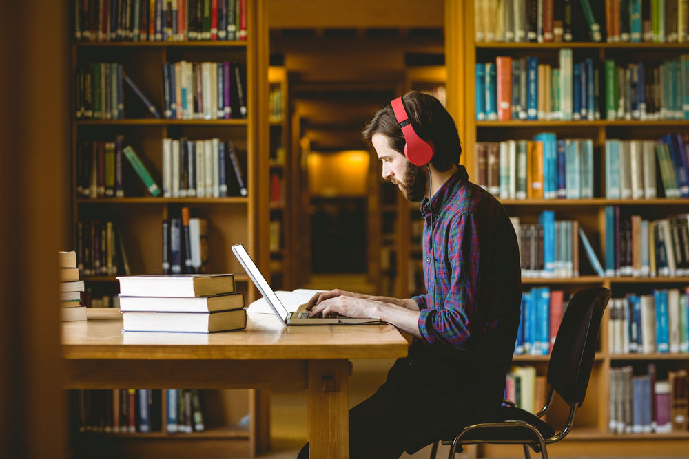 Student wearing headphones on laptop in library.