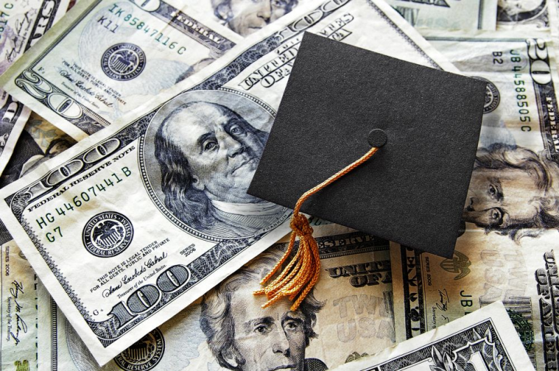 A graduation cap sitting on top of paper bills.