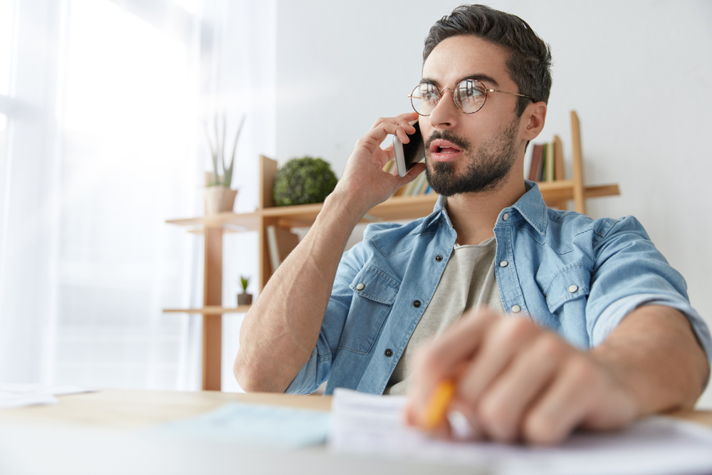 Young man talking on mobile phone at desk.