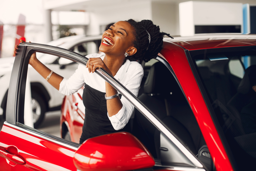 Woman smiling standing beside red car.