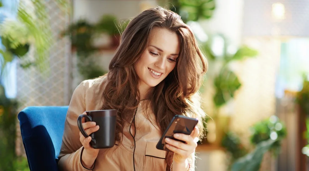 A woman drinking coffee and looking at her phone