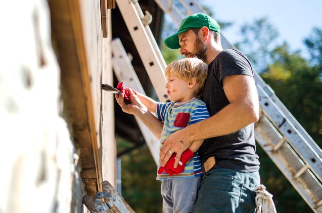 Son helping his dad paint a fence